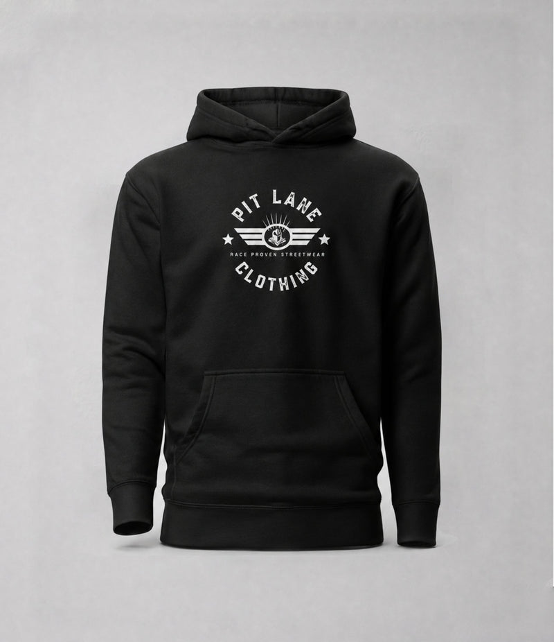 Close-up of a man wearing a black hooded sweatshirt, showing the side profile and a circular gray graphic on the upper left sleeve that reads 'PIT LANE CLOTHING' with 'TRACK TESTED' and 'RACE PROVEN'.