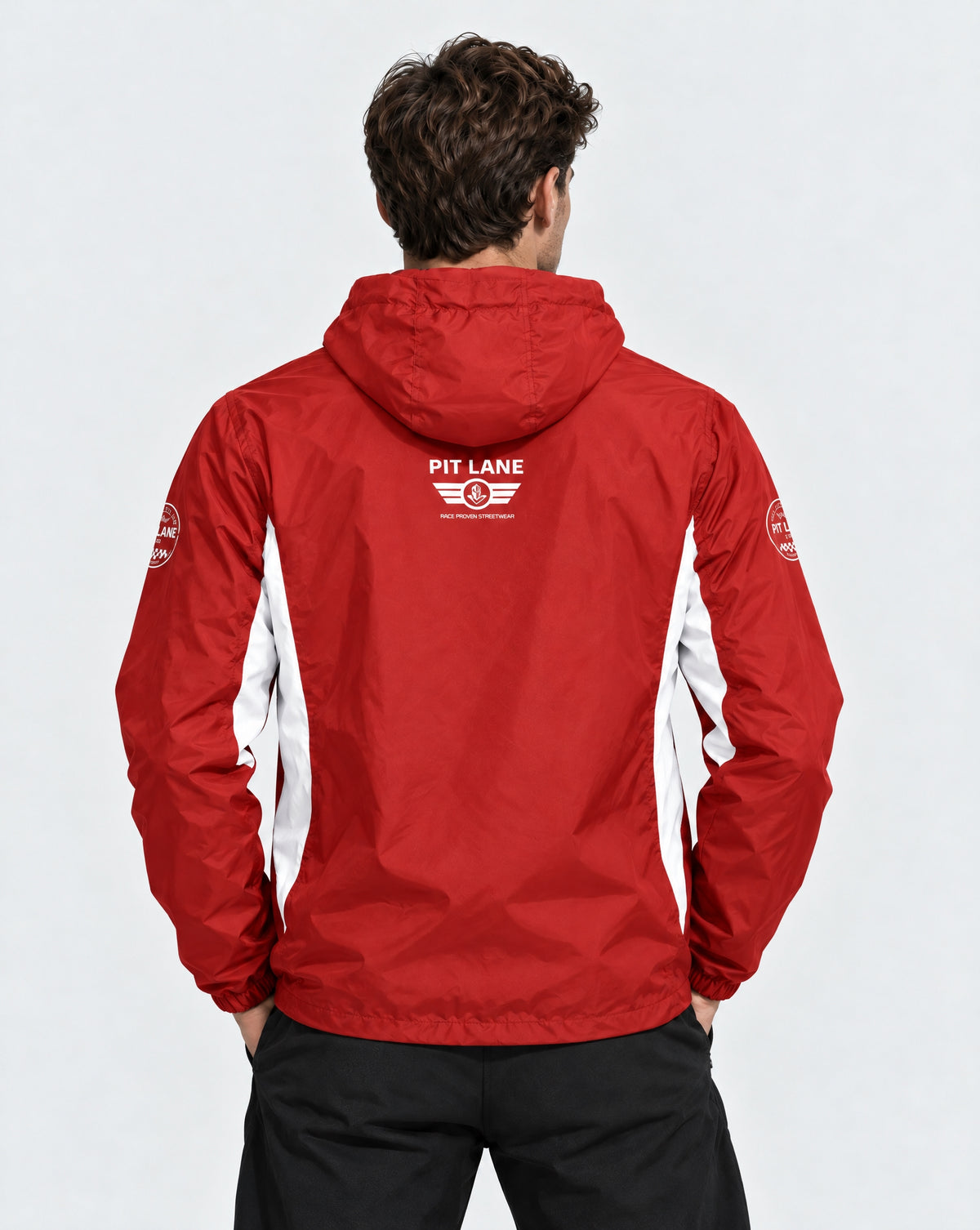A man viewed from behind wearing a red hooded jacket with white side panels and a white 'PIT LANE CLOTHING' logo on the back, paired with black pants against a light gray studio background.