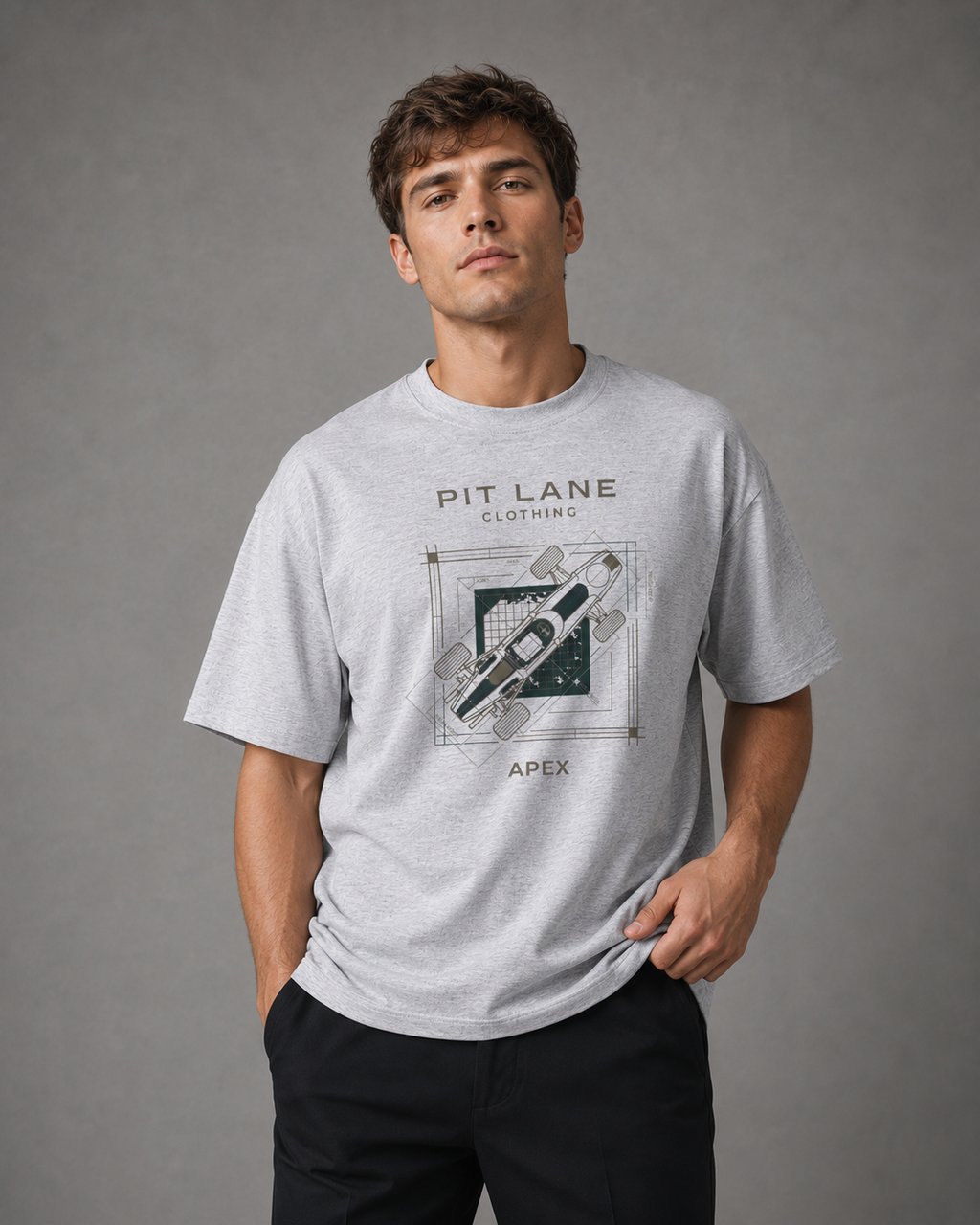 A man wearing a light gray heather crewneck t-shirt with a dark graphic print that reads 'PIT LANE CLOTHING' and 'APEX' around an illustration of a syringe. He is standing against a neutral gray studio background.