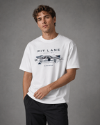 A man wearing a white crewneck t-shirt with a black graphic print of a race car and the text 'PIT LANE CLOTHING' and 'SLIPSTREAM' against a gray studio background.