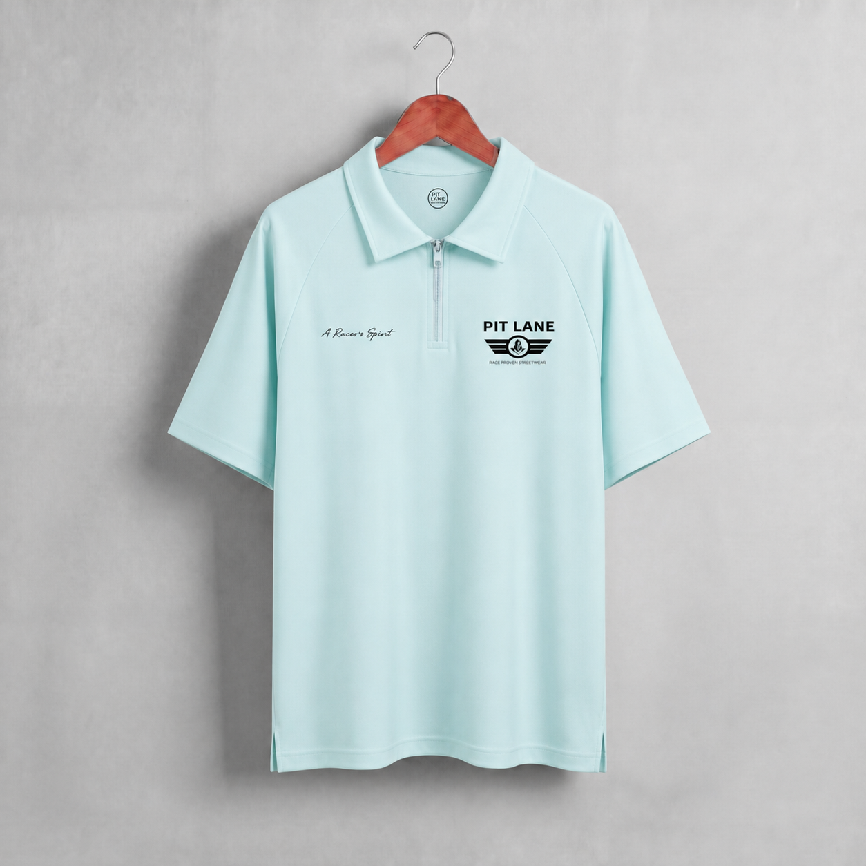 A light mint green short-sleeve polo shirt hanging on a wooden hanger against a textured gray wall. The shirt features a half-zip collar, a black 'PIT LANE' winged logo on the left chest, and a small black script logo on the right chest.
