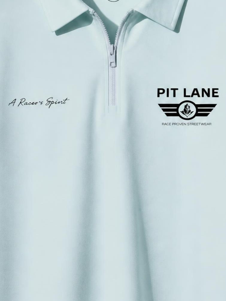 A close-up of a light mint green or pale aqua quarter-zip pullover top with a collar. The left chest has the script text 'A Racer's Spirit', and the right chest features the black 'PIT LANE' logo with wings and the text 'RACE PROVEN STREETWEAR'.