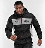 A man wearing a black and gray racing-inspired hooded jacket with '300 KPH' and 'PIT LANE' graphics, posed against a light gray studio background.