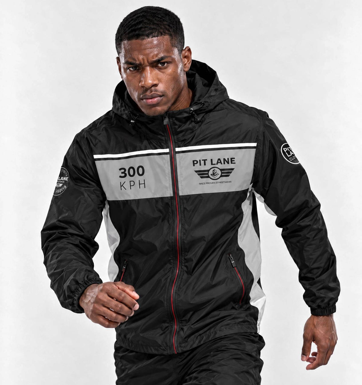 A man wearing a black and gray racing-inspired hooded jacket with '300 KPH' and 'PIT LANE' graphics, posed against a light gray studio background.