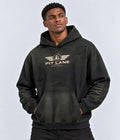 A man wearing a dark washed black Pit Lane Clothing hoodie with a distressed design and a gold chest logo, posed against a light gray studio background.