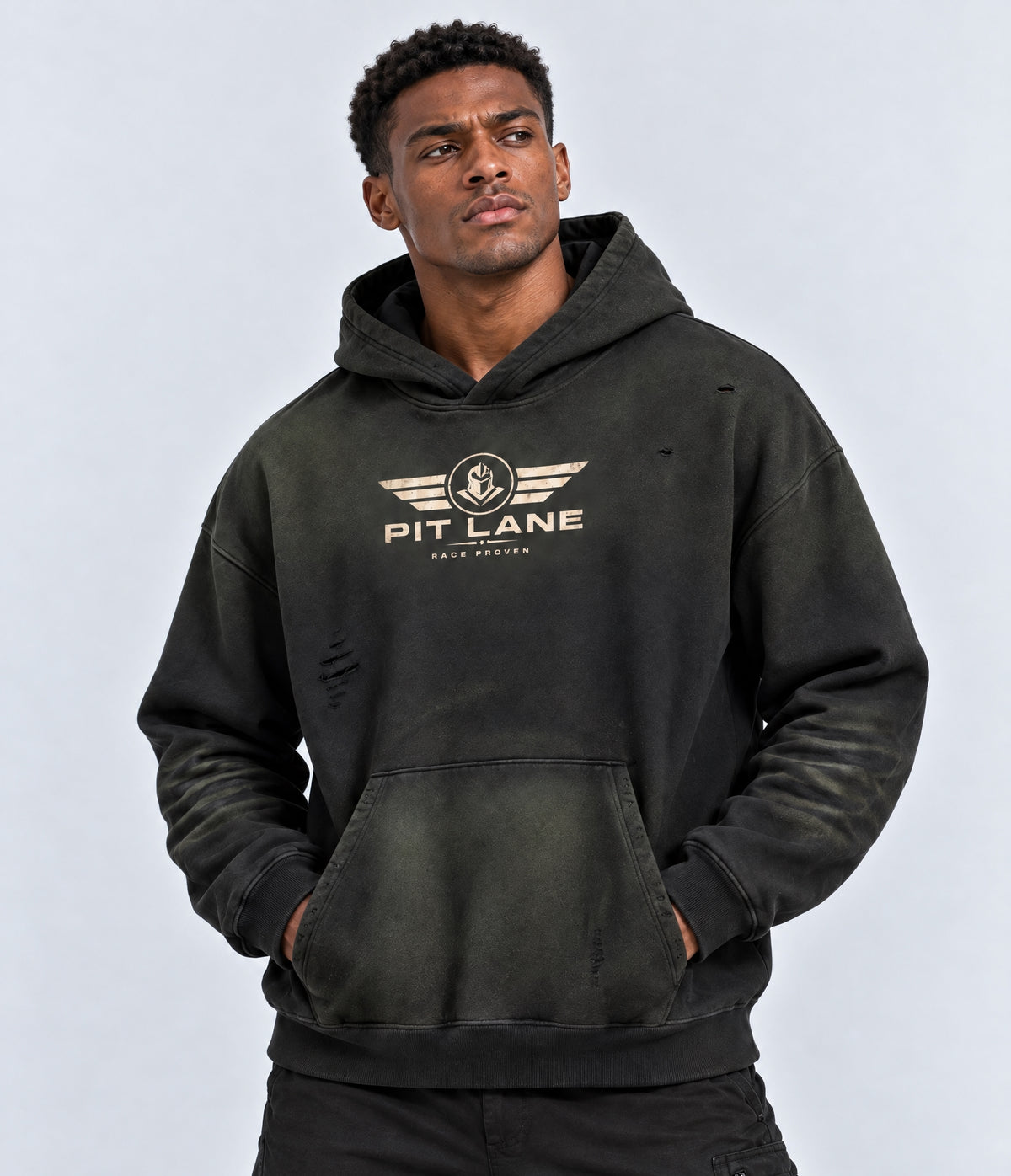 A man wearing a dark washed black Pit Lane Clothing hoodie with a distressed design and a gold chest logo, posed against a light gray studio background.