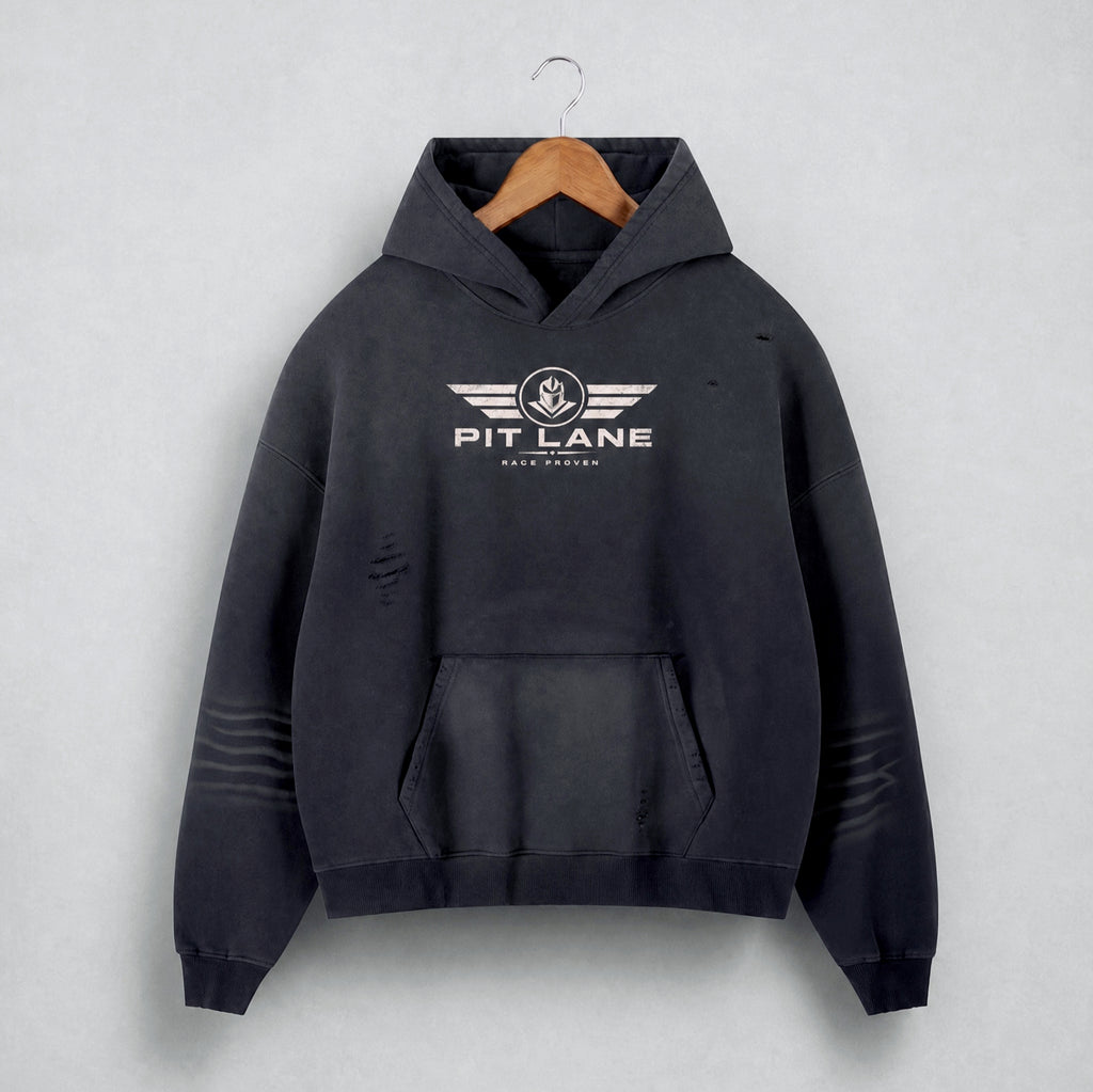 A black distressed hoodie with a white 'PIT LANE' winged logo on the chest, hanging on a wooden hanger against a light gray textured background.