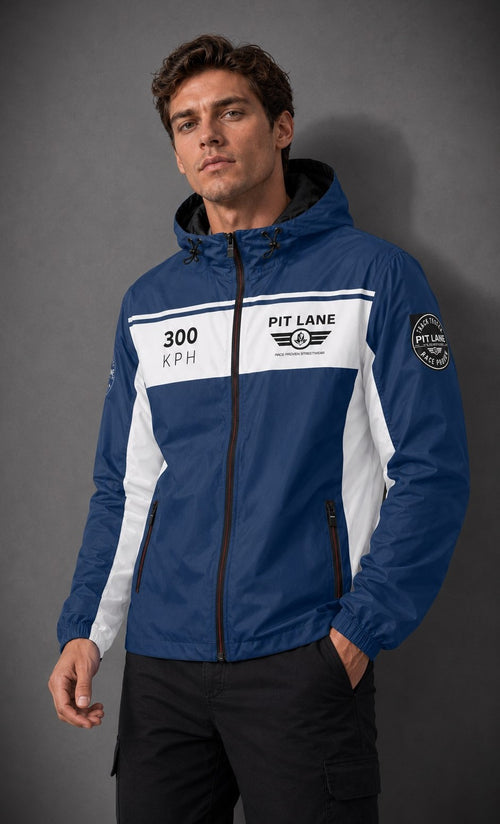 A man wearing a blue and white Pit Lane Clothing hooded jacket with black pants, standing against a dark gray studio background.