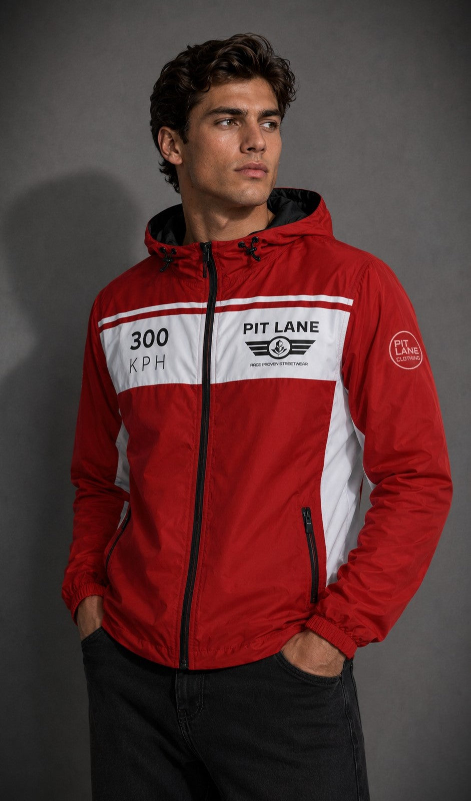 A man wearing a red and white hooded windbreaker jacket with 'PIT LANE CLOTHING ' and '300 KPH' graphics, posed against a dark gray studio background.