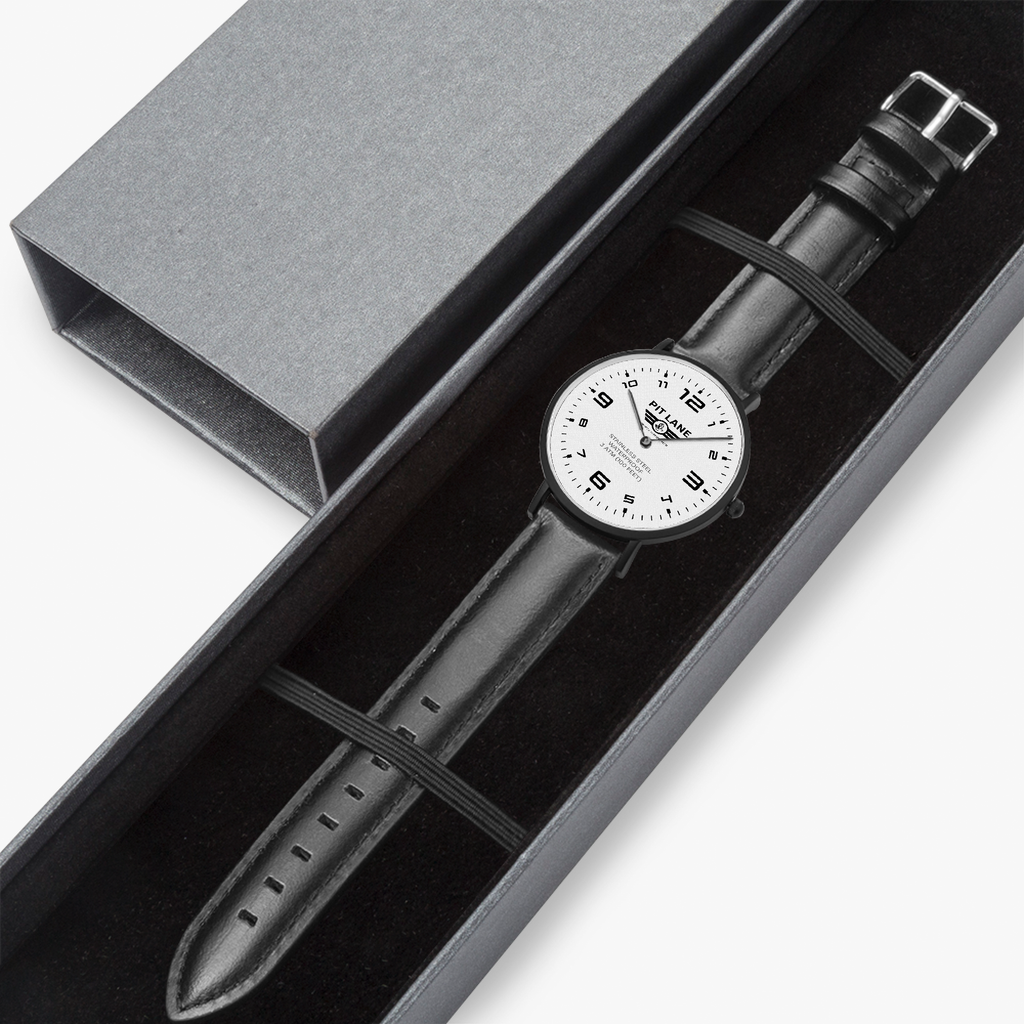 A Pit Lane wristwatch with a black leather strap, black case, and a white dial with black Arabic numerals, shown against a light gray background.