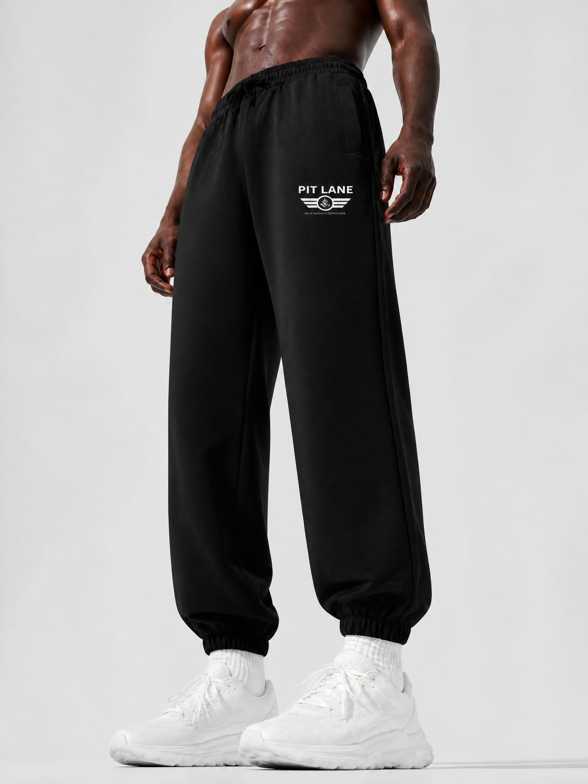 Black jogger sweatpants with a white 'PIT LANE' winged logo on the left thigh, modeled on a shirtless man wearing white sneakers against a light gray studio background.