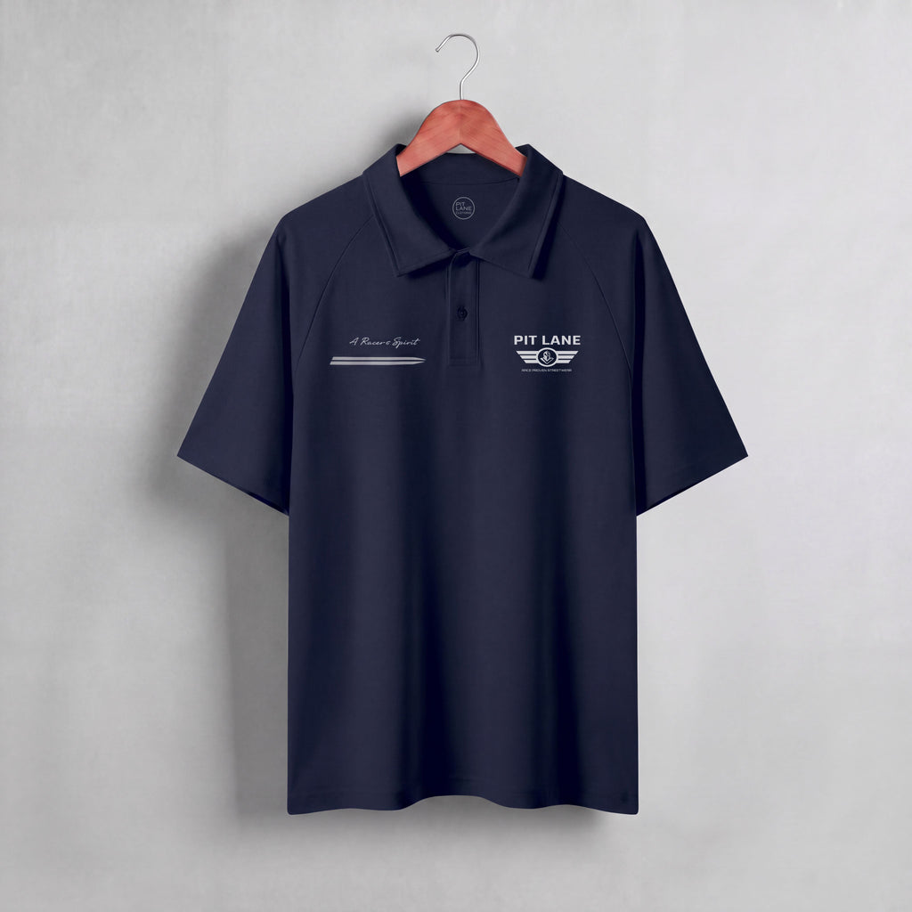 A dark navy blue short-sleeve polo shirt hanging on a wooden hanger against a light gray textured wall. The shirt features white embroidered graphics on the chest, including 'PIT LANE' with wings on the left chest and a script logo on the right chest.
