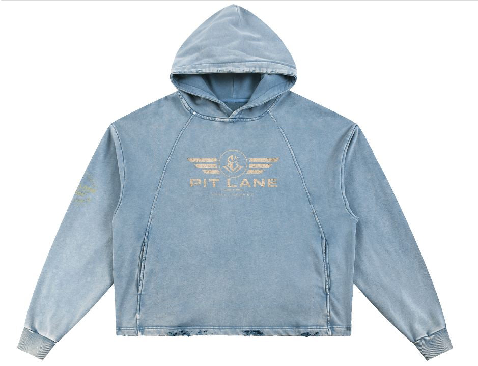 A light blue acid-wash cropped hoodie with a distressed gold 'PIT LANE' graphic printed on the chest, displayed against a solid white background.