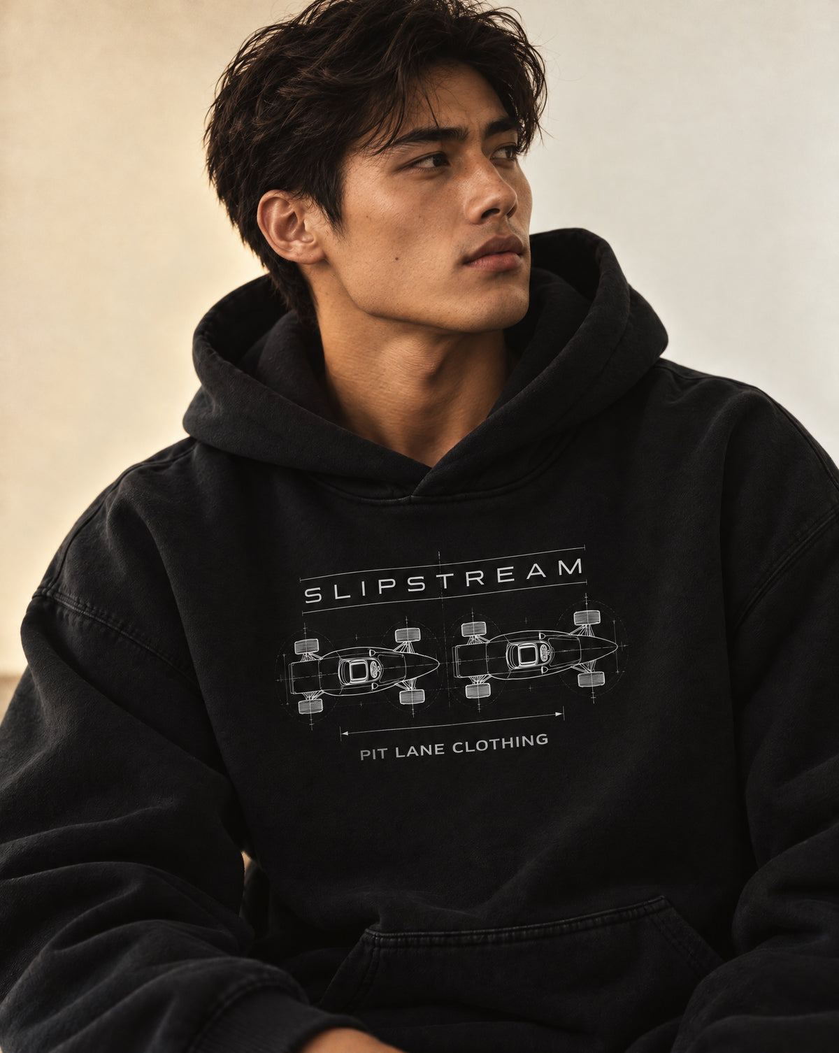 A black pullover hoodie with a white graphic print on the chest featuring the text 'SLIPSTREAM' and 'PIT LANE CLOTHING' with a technical schematic of two cars. The hoodie is displayed on a clean, light gray background.