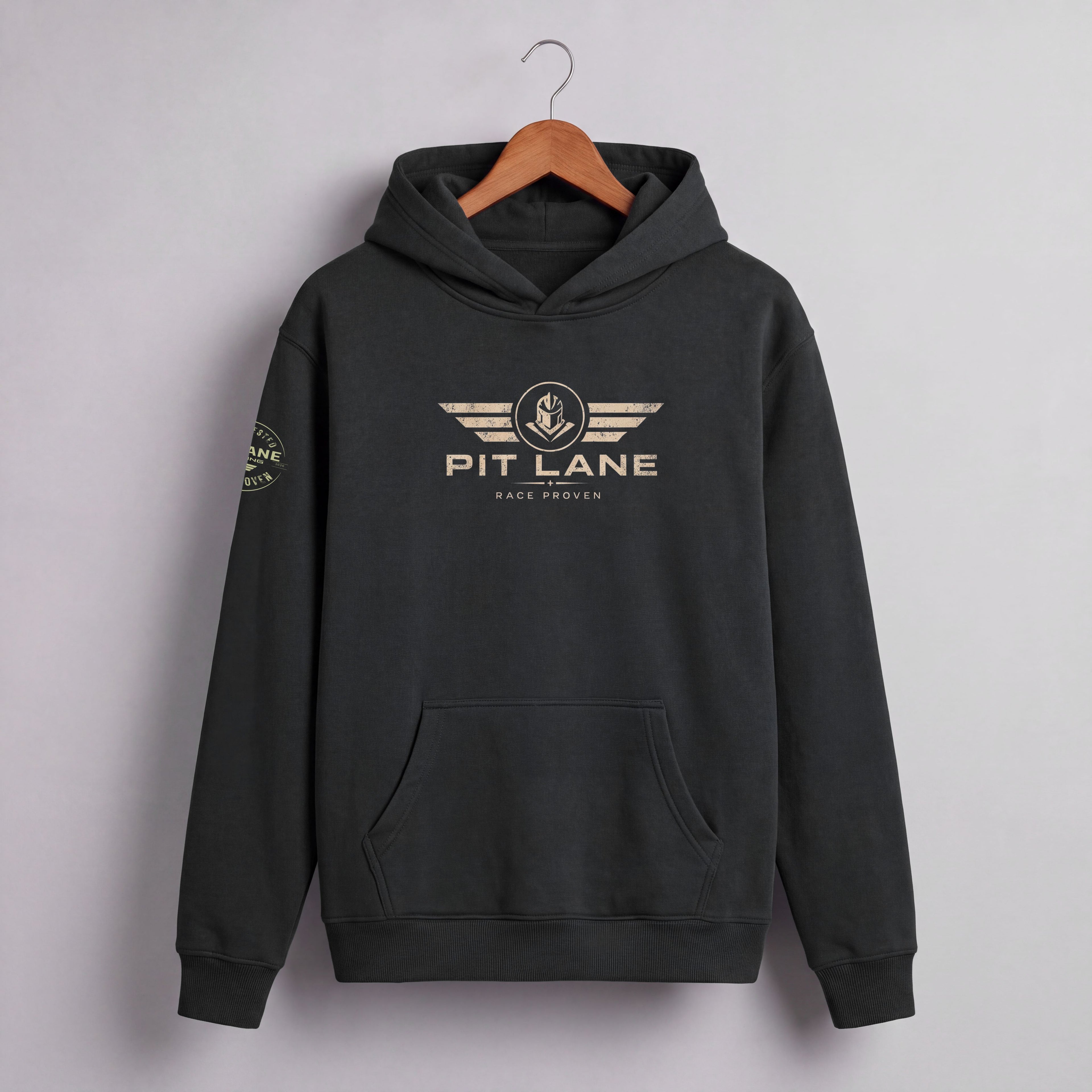 A dark charcoal gray pullover hoodie hanging on a wooden hanger against a light gray wall. The hoodie features a distressed gold graphic on the chest with the text 'PIT LANE' and 'RACE PROVEN' beneath it, and a matching circular graphic on the left sleeve.