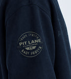 Close-up of a dark navy sweatshirt sleeve featuring a circular 'Pit Lane Clothing' graphic printed in a faded off-white color on the upper arm.