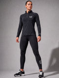 A woman modeling a dark gray heathered long-sleeve quarter-zip athletic top and black leggings with white PIT LANE CLOTHING branding, standing against a gray studio background.