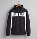 A black hooded windbreaker jacket with white side panels and a white chest stripe, hanging on a wooden hanger against a light gray background. The chest features '300 KPH' and 'PIT LANE CLOTHING' graphics.