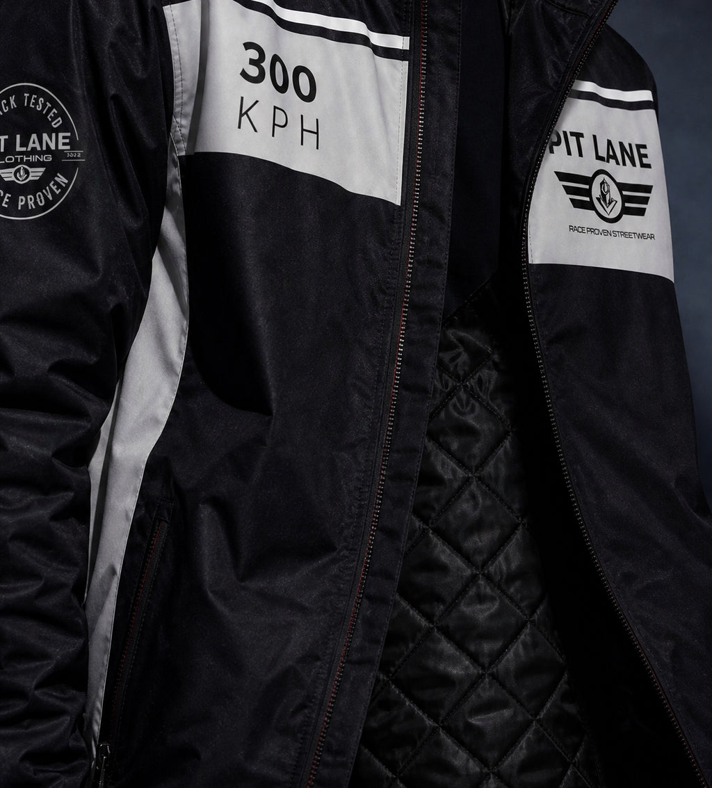 Close-up of a black jacket with white panels, featuring '300 KPH' and 'PIT LANE' branding, a quilted interior lining, and a circular sleeve patch.