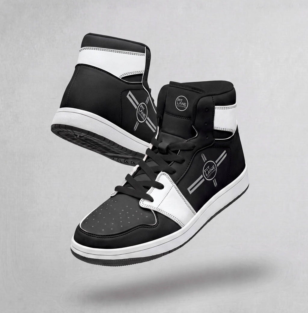 A pair of black and white PIT LANE CLOTHING high-top sneakers floating against a textured gray background. The sneakers feature a black leather upper with white panels, black laces, and a white midsole.