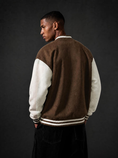 A man wearing a brown and off-white varsity jacket, shown from the back against a dark gray studio background.