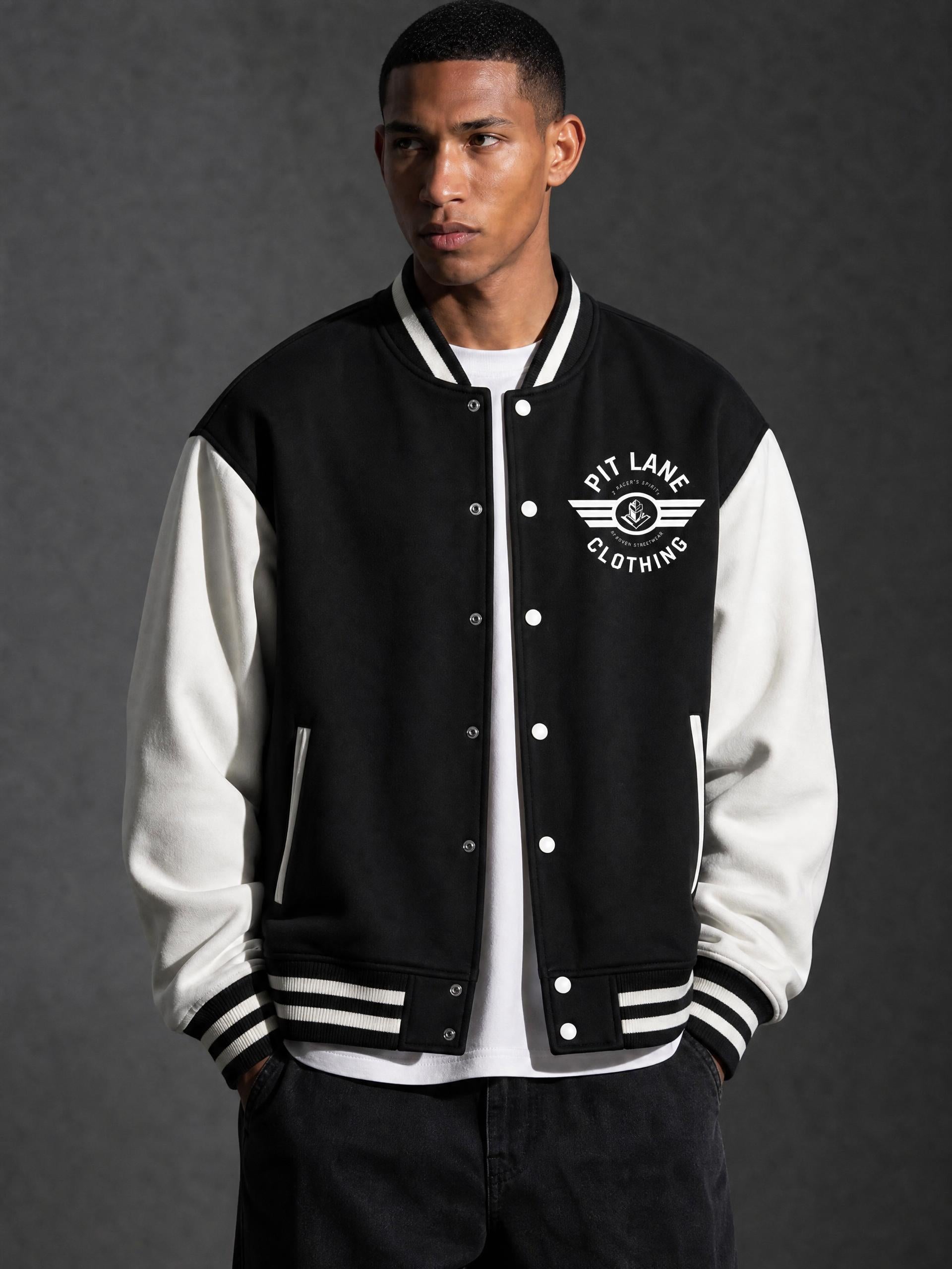 A man wearing a black and white varsity jacket with 'PIT LANE CLOTHING' embroidered on the chest, posed against a dark gray studio background.