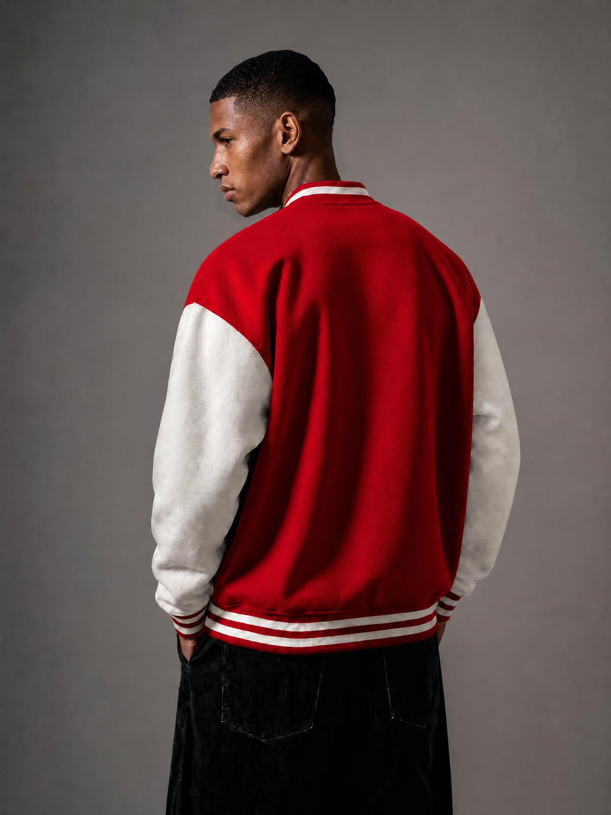 A man wearing a red and white varsity jacket, photographed from the back against a neutral gray studio background.
