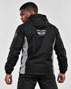 A man wearing a black hooded windbreaker jacket with gray side panels and white 'PIT LANE' branding on the back, shown from behind against a light gray studio background.