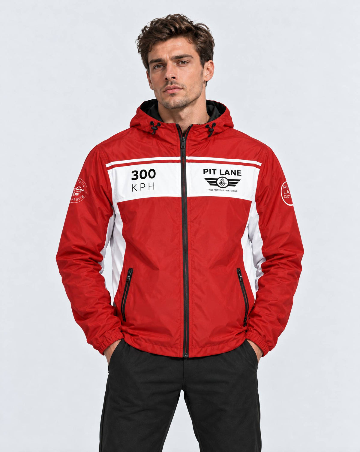 A man wearing a red and white hooded jacket with 'PIT LANE CLOTHING' and '300 KPH' graphics, paired with black pants, against a light gray studio background.