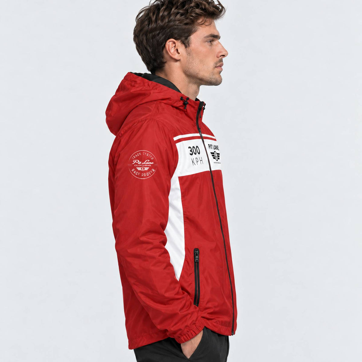 A man in profile wearing a red and white PIT LANE CLOTHING jacket with black zippers and white printed graphics, photographed against a light gray studio background.