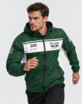 A man wearing a green and white PIT LANE CLOTHING windbreaker jacket, posed in a running stance against a light gray studio background.