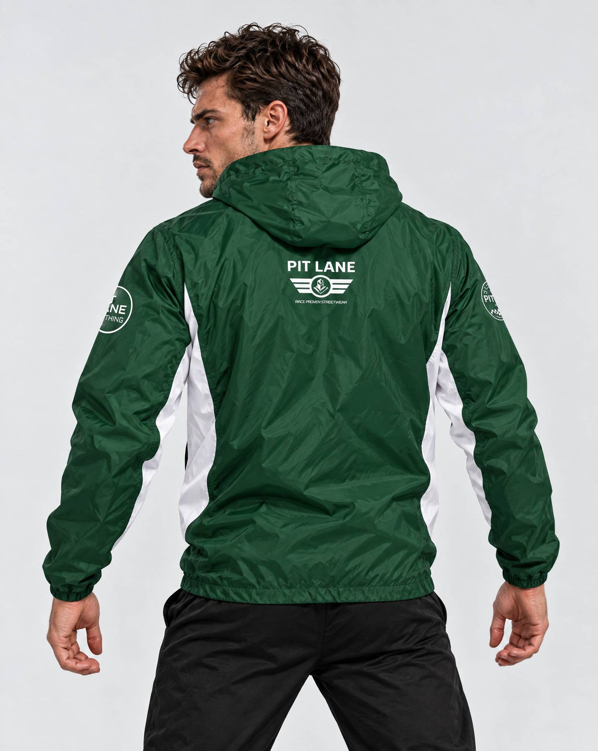 A man wearing a green and white hooded windbreaker jacket, shown from the back. The jacket features 'PIT LANE CLOTHING' branding printed in white on the upper back and a circular logo on the right sleeve.
