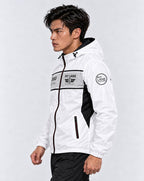 A man wearing a white hooded windbreaker jacket with black and gray racing-style graphics and 'PIT LANE CLOTHING' branding, paired with black pants, against a light gray studio background.