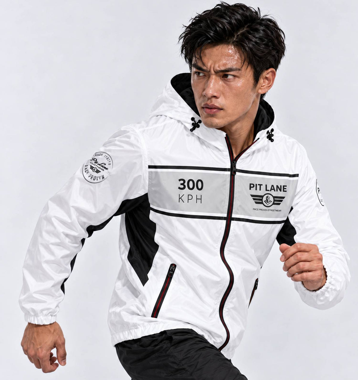 A man wearing a white, black, and gray windbreaker jacket with '300 KPH' and 'PIT LANE CLOTHING' graphics, posed dynamically against a light gray studio background.