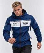 A man wearing a navy blue and white hooded windbreaker jacket with 'PIT LANE' and '300 KPH' printed on the chest, posed against a light gray studio background.
