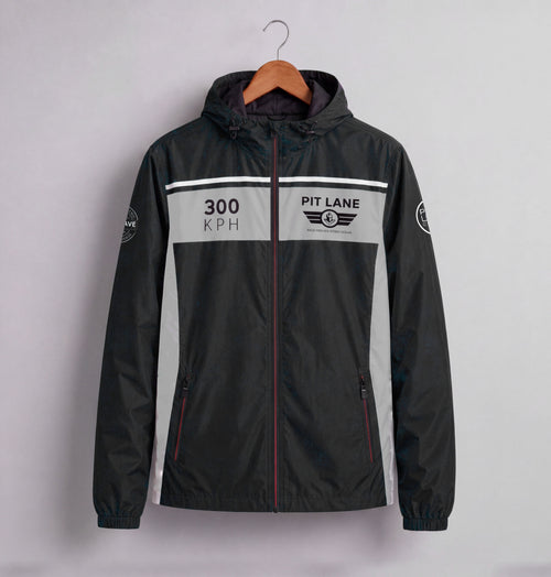 A black hooded windbreaker jacket with a gray chest panel and white racing-style graphics, hanging on a wooden hanger against a light gray wall. The chest reads '300 KPH' and 'PIT LANE CLOTHING' with a winged logo.