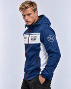 A man wearing a blue and white hooded windbreaker jacket with 'PIT LANE' branding on the chest and sleeve, posed against a light gray studio background.