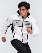 A man wearing a white and black windbreaker jacket with '300 KPH' and 'PIT LANE CLOTHING' printed on the chest, posed dynamically against a light gray studio background.