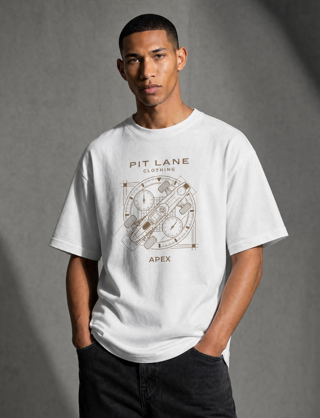 A man wearing a white short-sleeve graphic t-shirt with a brown geometric design and text reading 'PIT LANE CLOTHING' and 'APEX', paired with dark jeans, standing against a textured gray studio background.