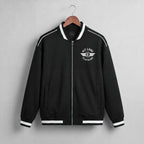 A navy blue zip-up jacket with white contrast stitching, ribbed collar, cuffs, and hem, hanging on a wooden hanger against a light gray textured wall. The left chest features a white circular logo reading 'KIT LANE CLOTHING' with a winged emblem.