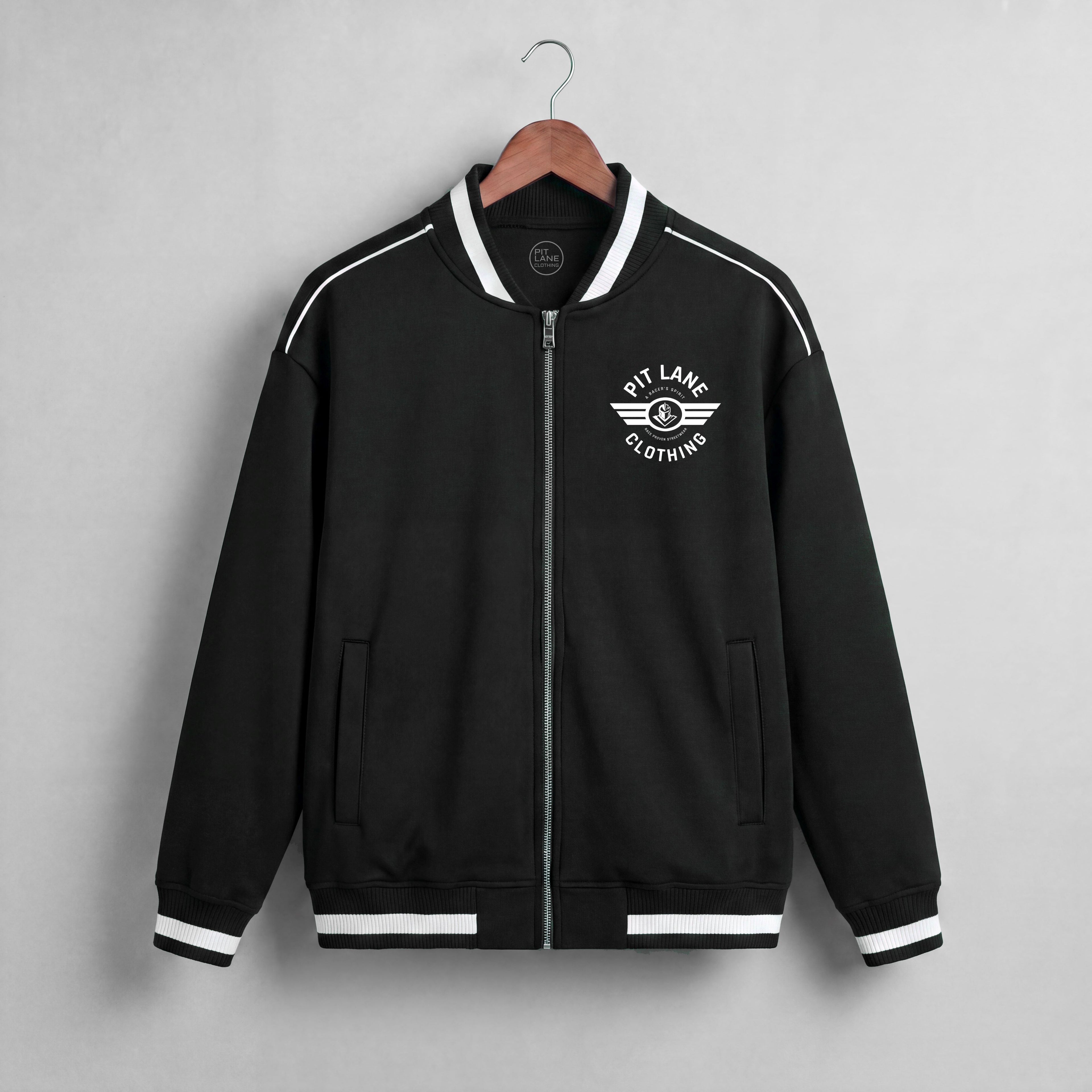 A navy blue zip-up jacket with white contrast stitching, ribbed collar, cuffs, and hem, hanging on a wooden hanger against a light gray textured wall. The left chest features a white circular logo reading 'KIT LANE CLOTHING' with a winged emblem.