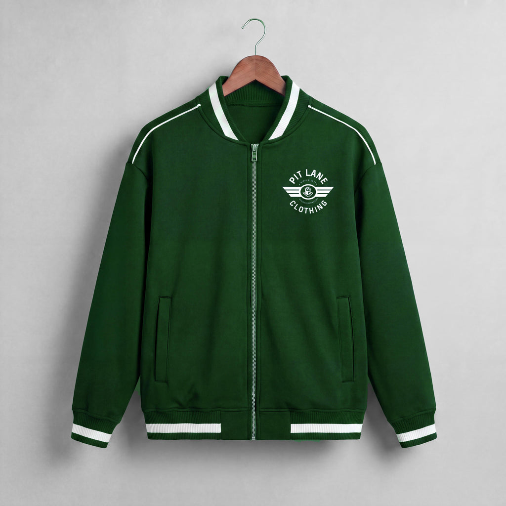 A dark green zip-up jacket with white contrast stitching, ribbed collar, cuffs, and hem, hanging on a wooden hanger against a light gray wall. The left chest features a white circular winged logo that reads 'PIT LANE CLOTHING'.