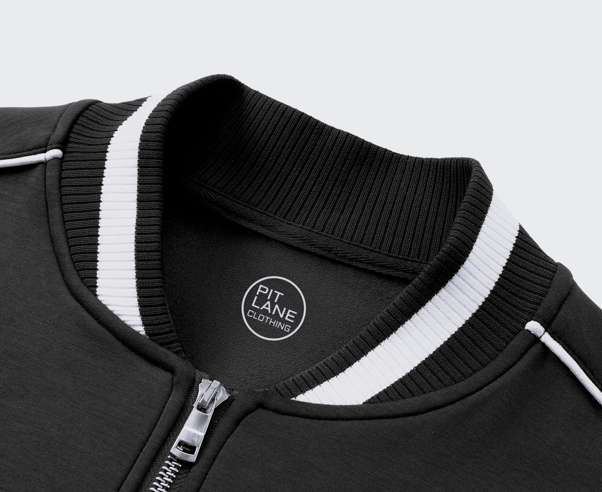 A navy blue zip-up jacket with white contrast stitching, ribbed collar, cuffs, and hem, hanging on a wooden hanger against a light gray textured wall. The left chest features a white circular logo reading 'KIT LANE CLOTHING' with a winged emblem.