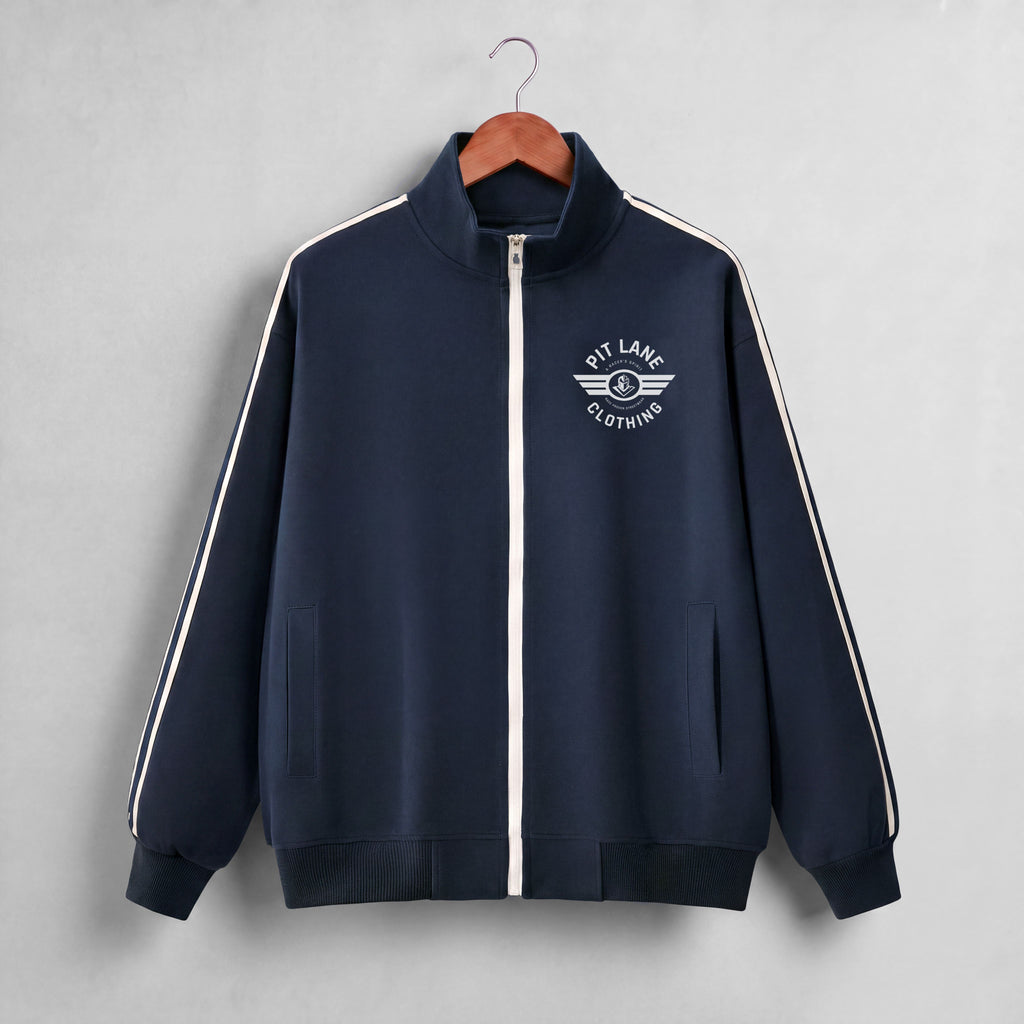 A navy blue zip-up track jacket with white shoulder stripes and a white chest logo reading 'PIT LANE CLOTHING', hanging on a wooden hanger against a light gray background.