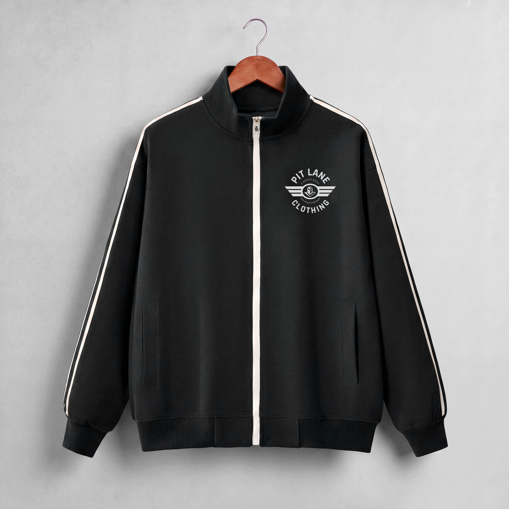 A black zip-up track jacket with a white front zipper, white shoulder stripes, and a white 'PIT LANE CLOTHING' wing logo on the chest, hanging on a wooden hanger against a light gray background.