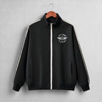 A black zip-up track jacket with a white front zipper, white shoulder stripes, and a white 'PIT LANE CLOTHING' wing logo on the chest, hanging on a wooden hanger against a light gray background.