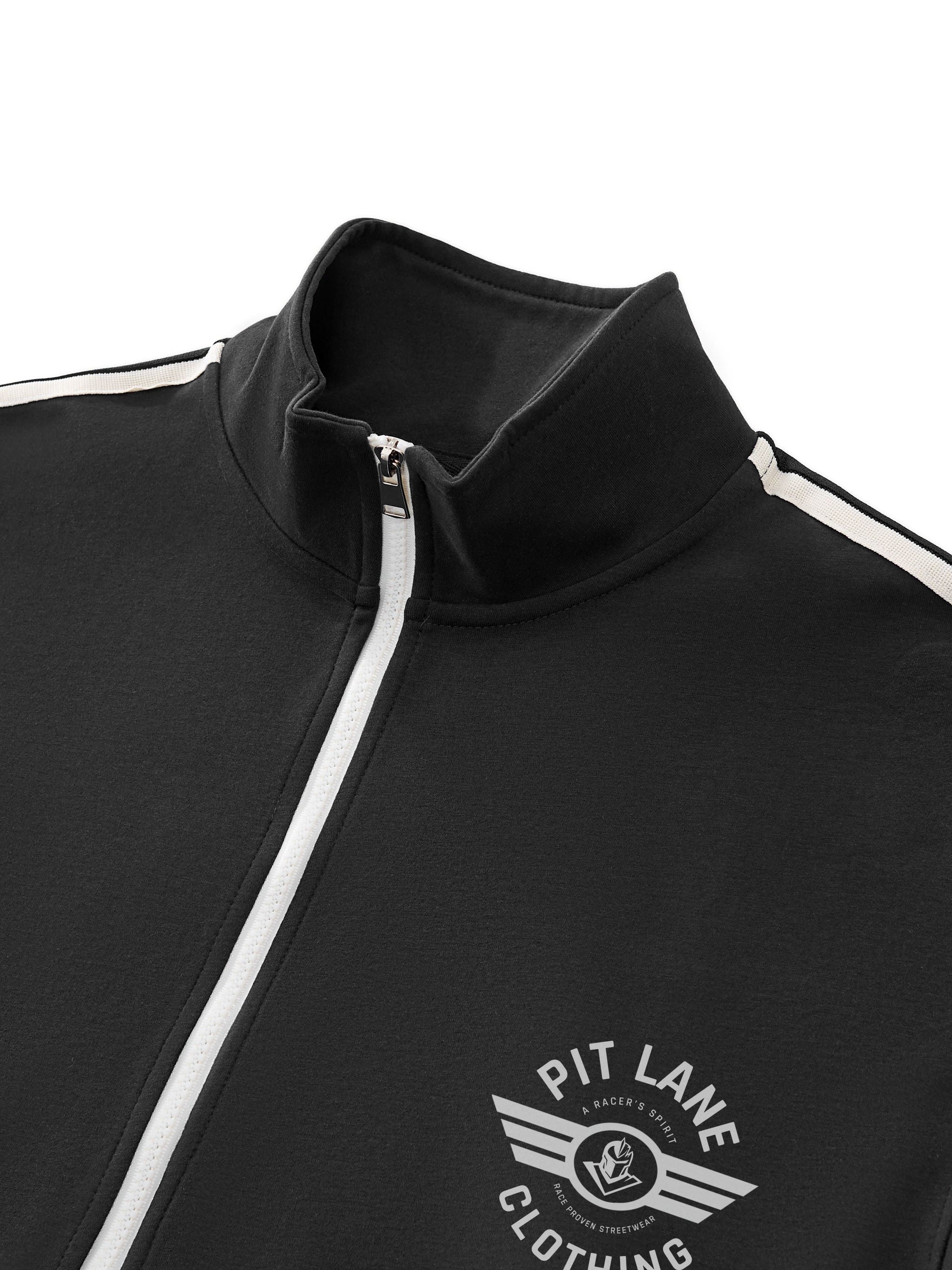Close-up of a black zip-up track jacket with a high collar, white zipper, and white shoulder stripes. A white 'PIT LANE CLOTHING' wing logo is printed on the left chest.