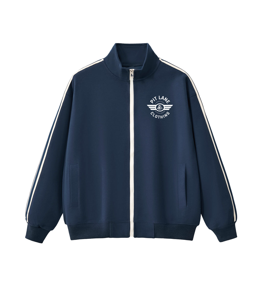 A navy blue zip-up track jacket with white shoulder stripes and a white chest logo reading 'PIT LANE CLOTHING', hanging on a wooden hanger against a light gray background.