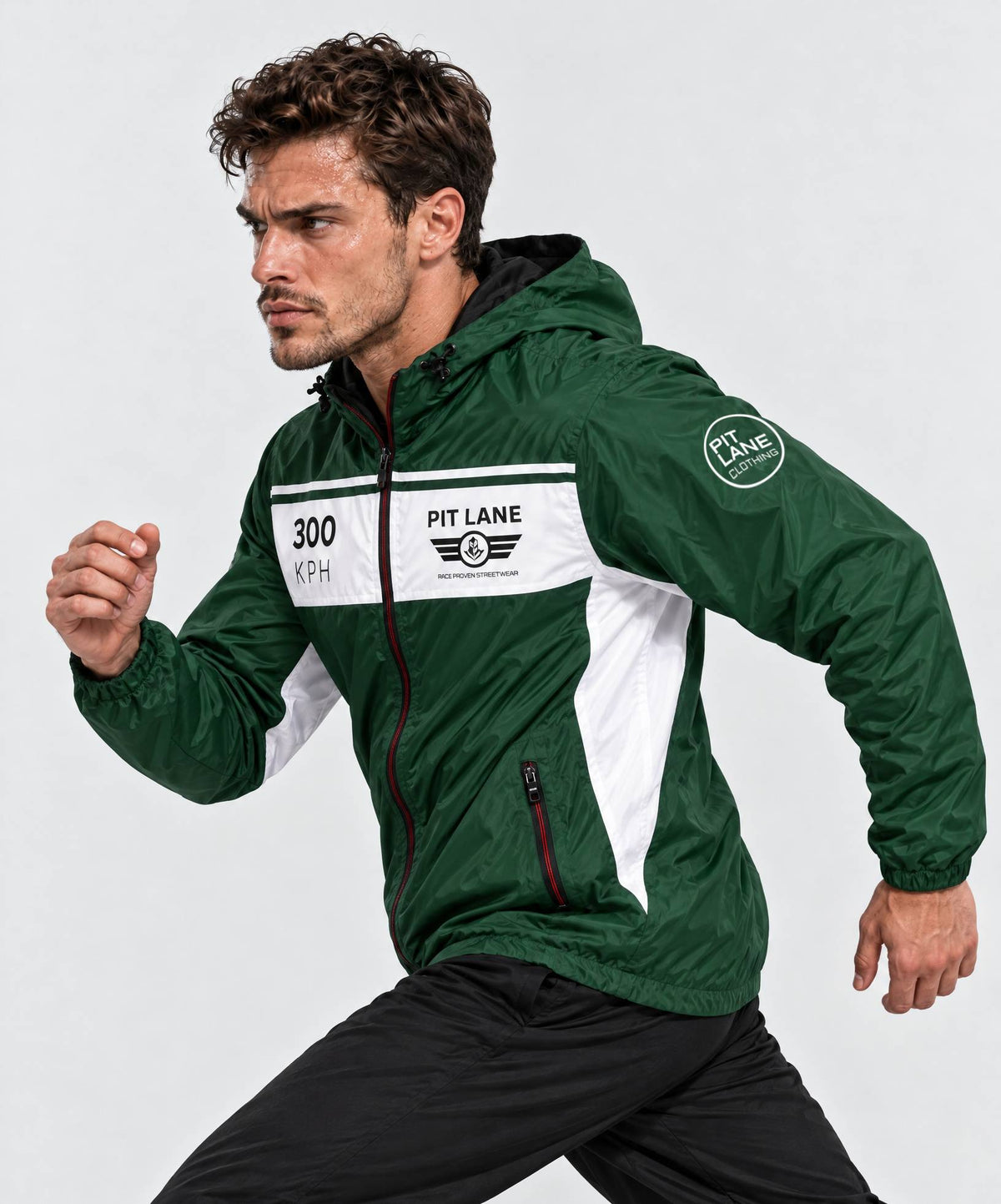 A man wearing a green and white PIT LANE CLOTHING windbreaker jacket, posed in a running stance against a light gray studio background.