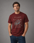 A man wearing a maroon short-sleeve graphic t-shirt with a white and gray track diagram and text reading 'PIT LANE CLOTHING' and 'LAP RECORD', paired with blue jeans, standing against a neutral gray studio background.